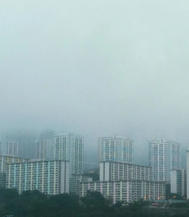 n DHA Lahore, tall, modern buildings rise amidst fog, with a majestic mountain backdrop.